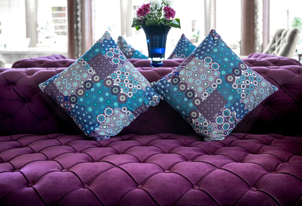 Purple velvet fabric modern sofa with sunken buttons and colorful decorative pillows ,ideal for interior design in Delhi, showcasing elegant cushion styles.